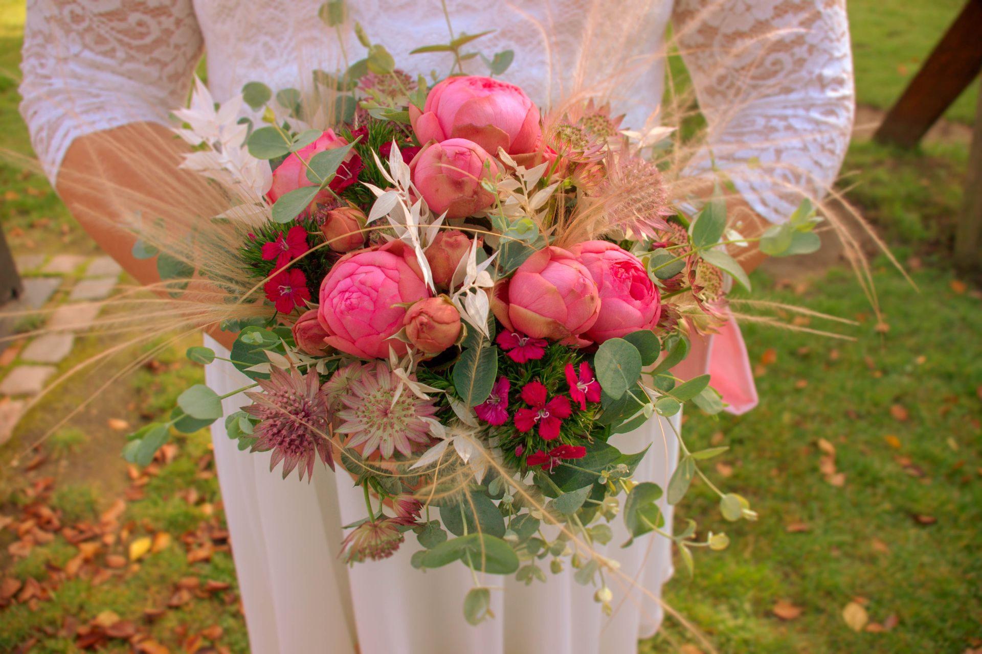Close-up of a bride holding a beautiful bouquet with vibrant pink peonies outdoors.