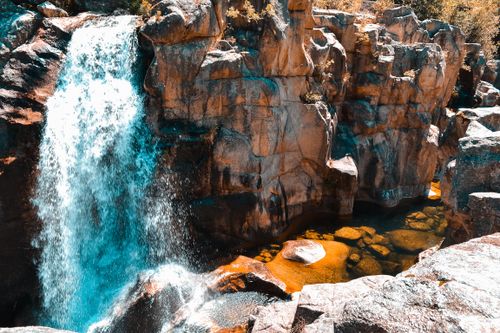 Free Sunlit waterfall cascading over rocky cliffs into a clear pool in a natural setting. Stock Photo