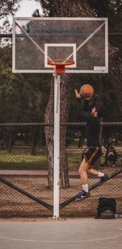 A basketball player makes a jump shot in an urban outdoor court.