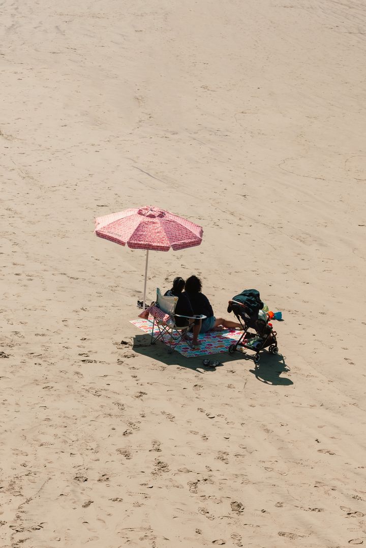 Familia a la sombra de una sombrilla en la playa con carrito cercano