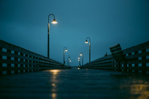 Rainy evening on a wooden pier with dim street lamps and reflections.