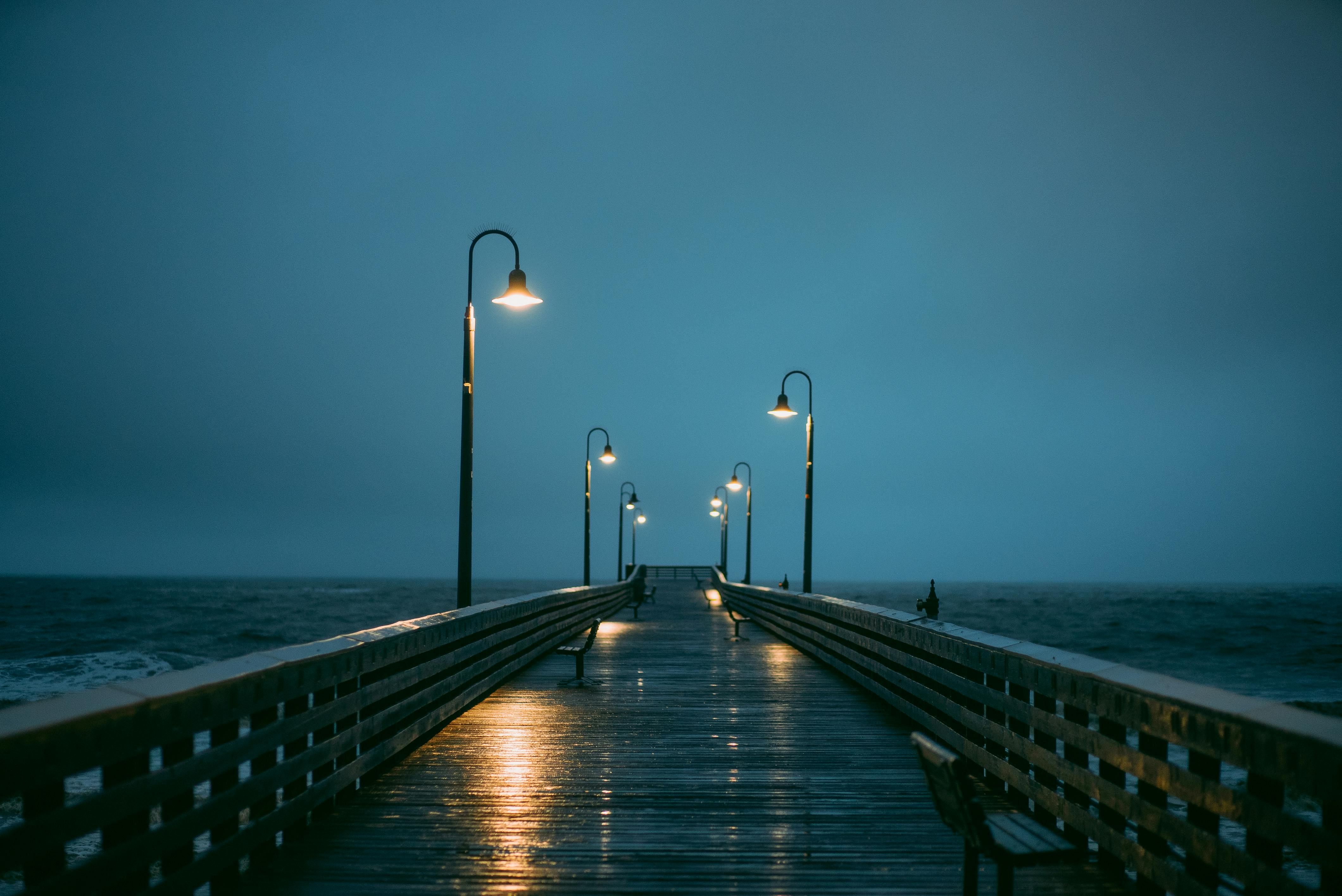 A moody and peaceful pier scene with glowing street lamps on an overcast evening by the sea.