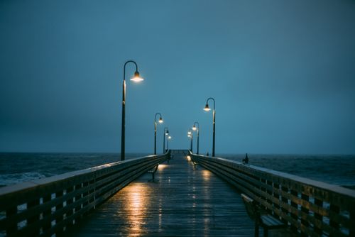 Free A moody and peaceful pier scene with glowing street lamps on an overcast evening by the sea. Stock Photo