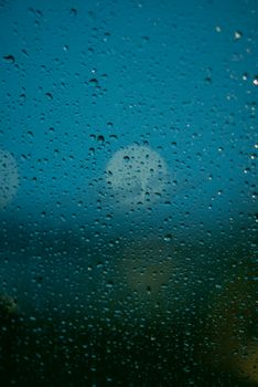 Close-up of raindrops on a window with a blurred moonlit night sky in the background.