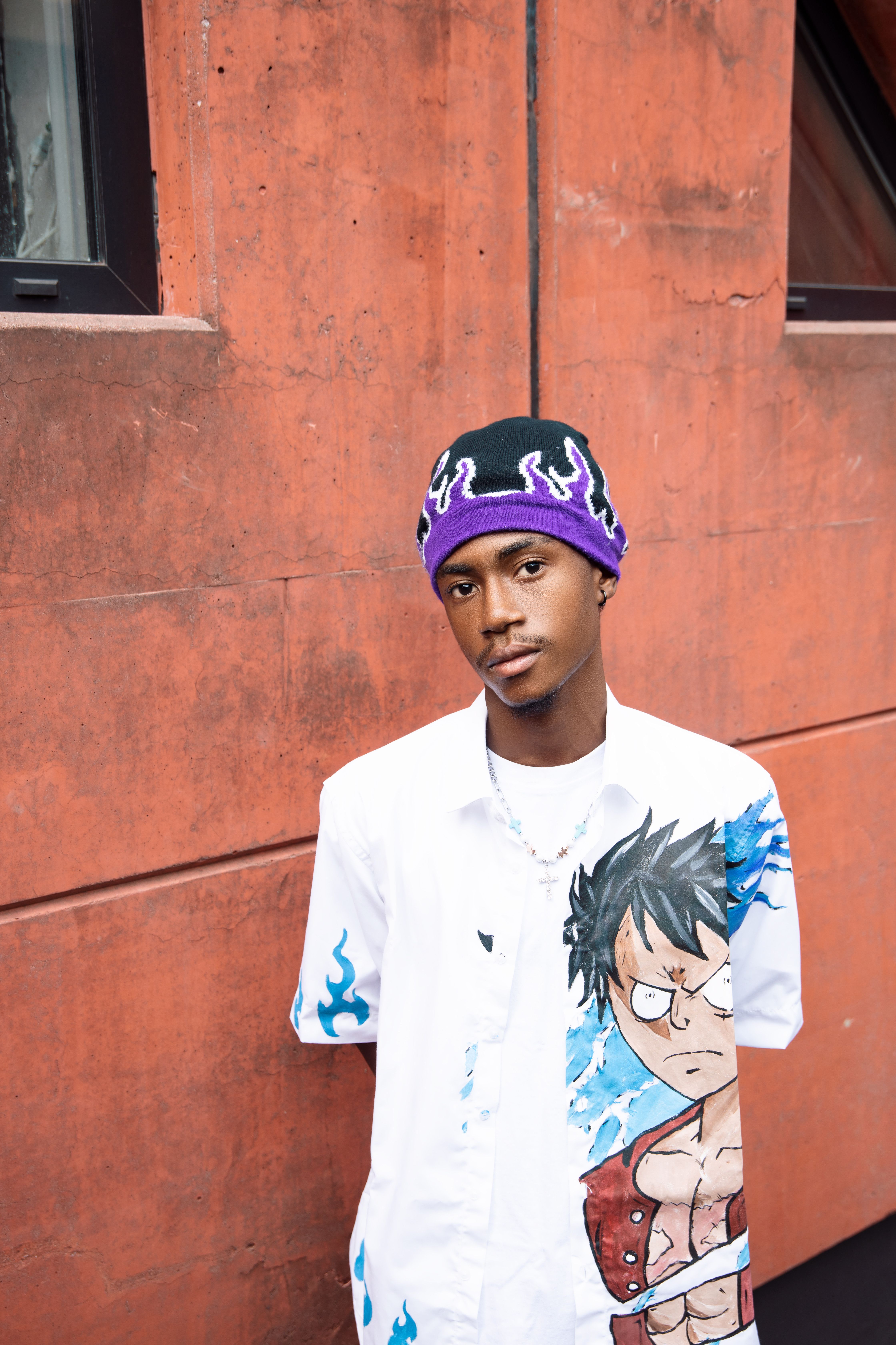 Young man in trendy streetwear and flame hat posing outdoors against an urban background.
