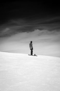 Black and white photo of a man snowboarding on a snowy mountain under cloudy skies.
