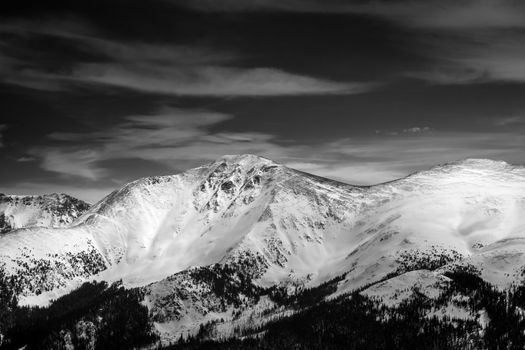 A stunning black and white aerial view of snowy mountains under a cloudy sky.