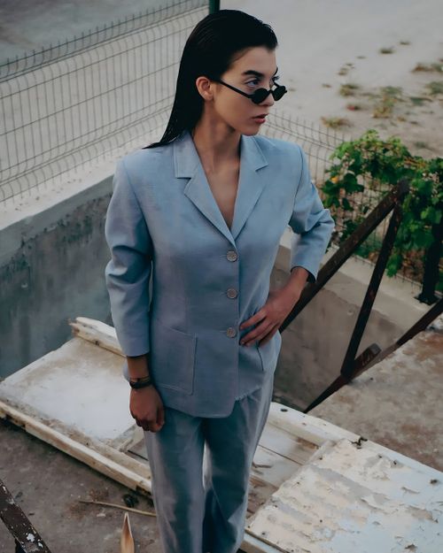 Free Fashion-forward woman in light blue suit and sunglasses stands outdoors with confident pose. Stock Photo