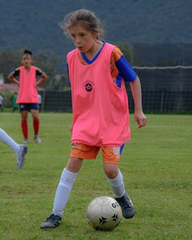A young girl focused on dribbling a soccer ball in a team practice session outdoors.