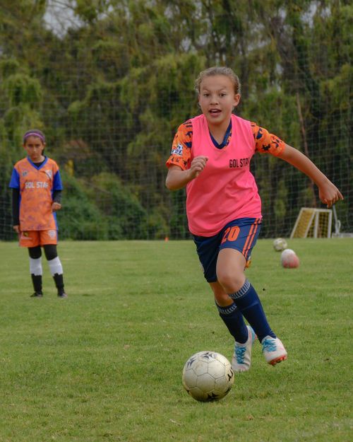 Free Energetic young girls engaged in a soccer match on a grassy field, showcasing teamwork and athleticism. Stock Photo