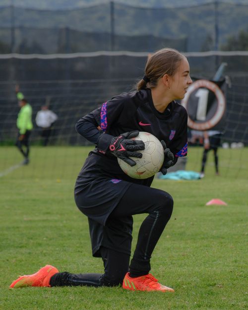 Free Young female goalkeeper in sports gear training with a ball on a grassy field. Stock Photo