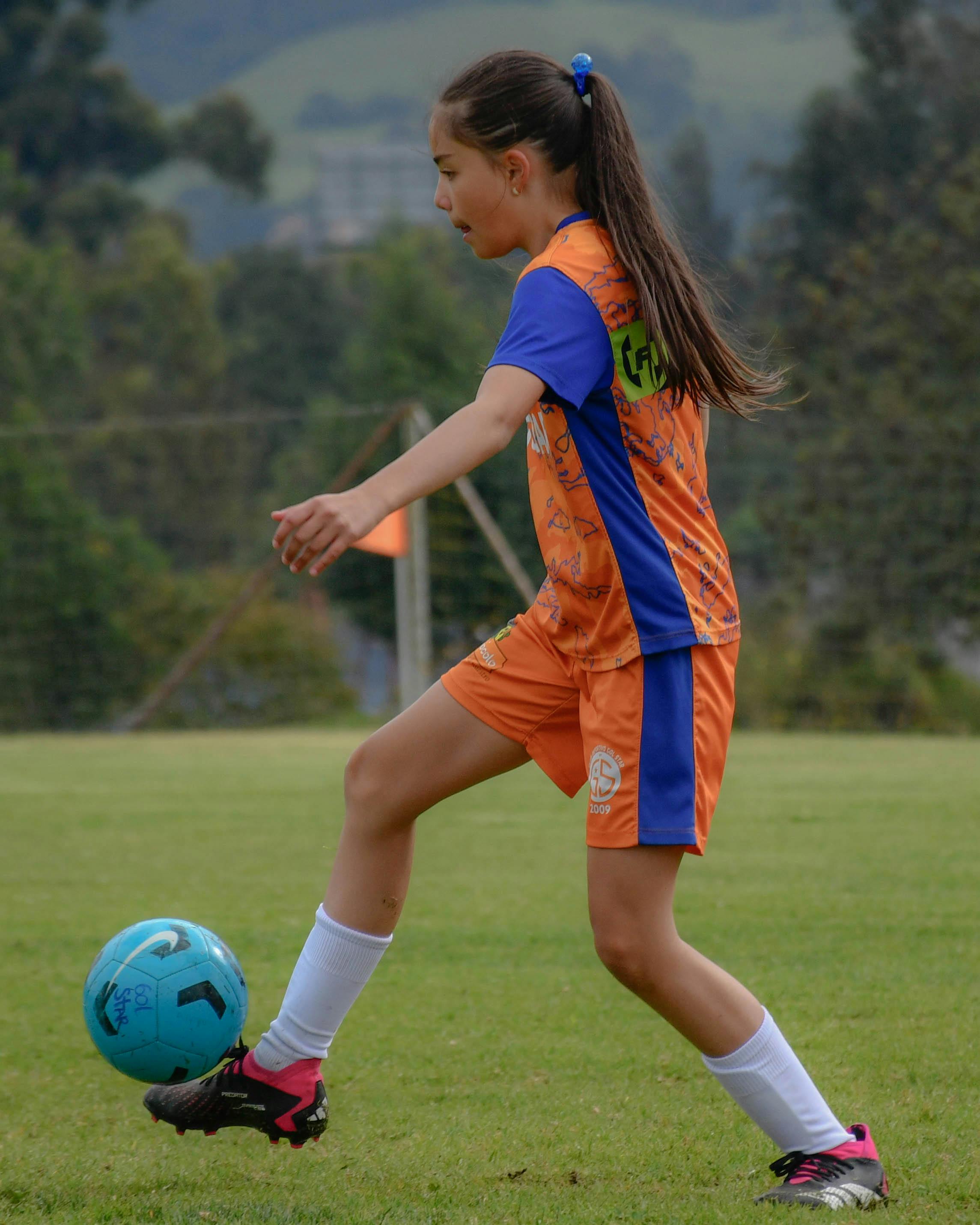A teenage girl in sportswear playing soccer outdoors on a green field.