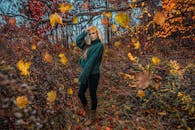 一位美丽的金发女子穿着厚厚毛衣，站在森林飘落的秋叶中