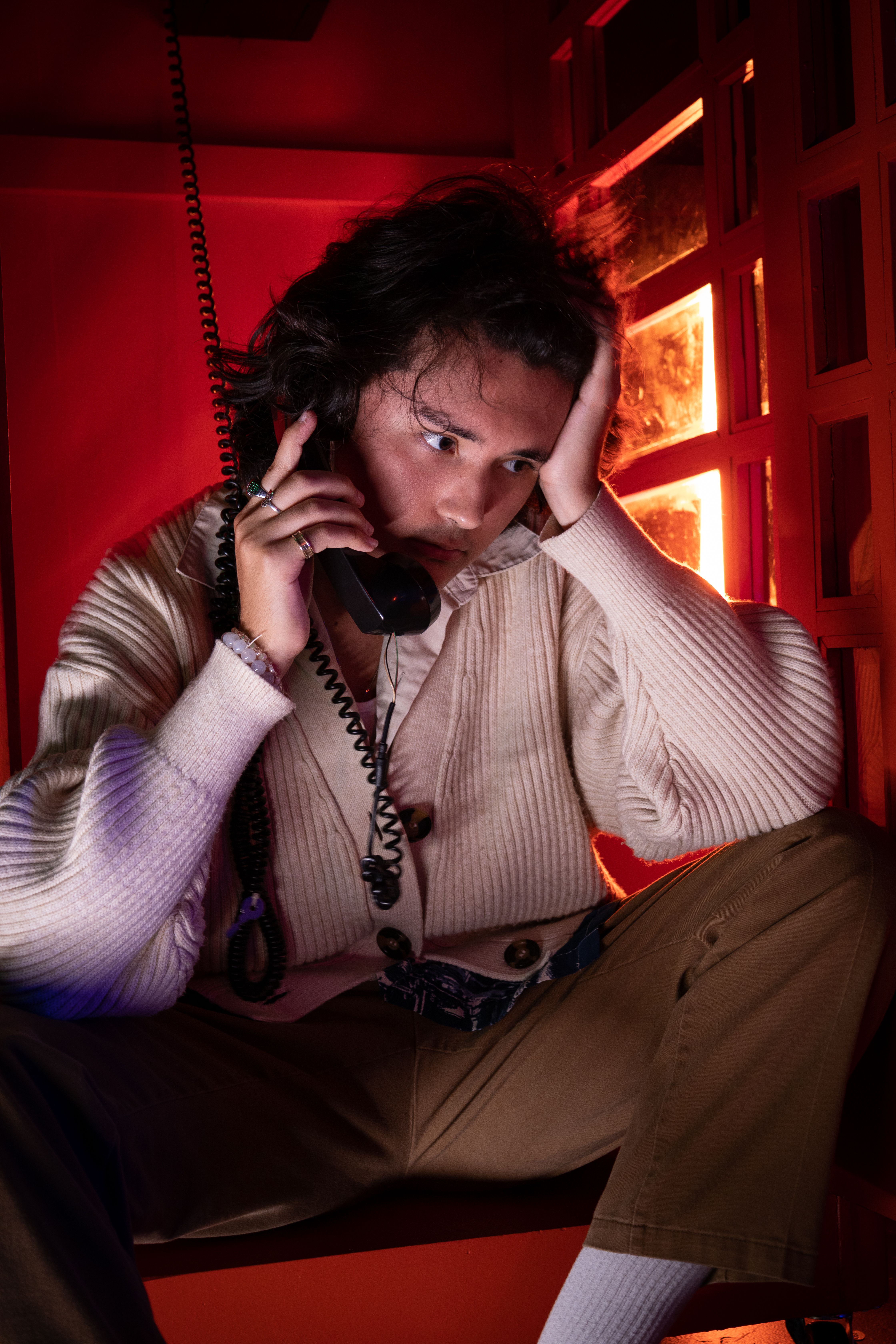 Portrait of a young man with intense expression talking on a phone in a moody, red-lit room.