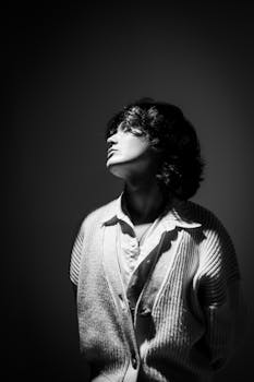 Black and white portrait of an adult wearing a sweater, looking upwards in dramatic lighting.