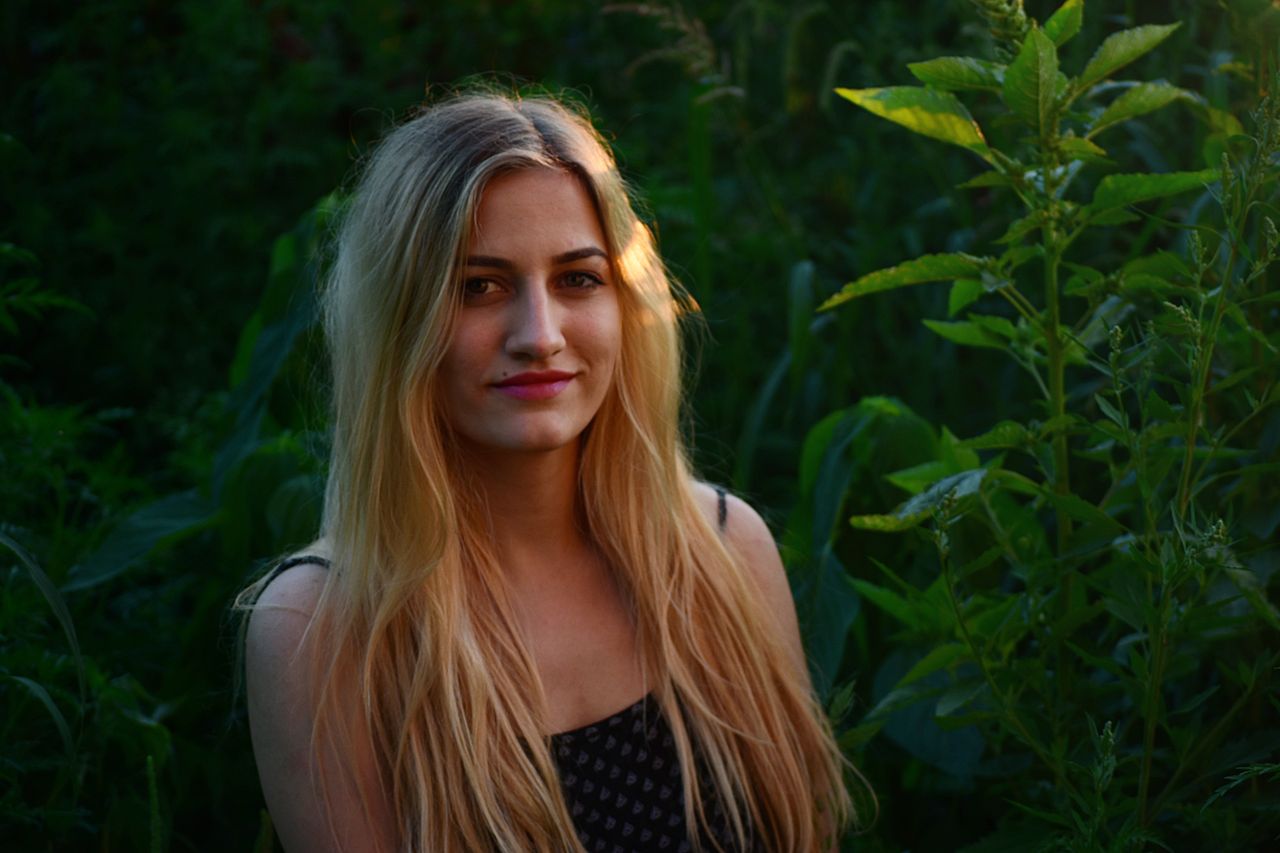 a beautiful blonde woman smiling in a natural outdoor setting with lus