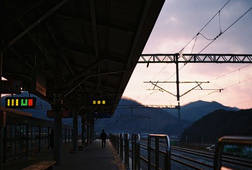 Free Dusk at a railway station with a silhouetted figure on the platform and colorful sky. Stock Photo