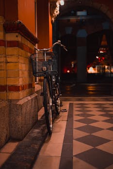 A vintage bicycle leans against a building wall under the warm evening lights of a city alleyway.