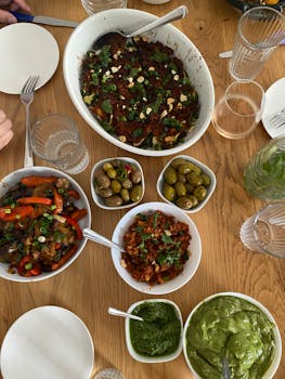 A variety of Mediterranean dishes on a wooden table, including bowls of olives, salads, and vibrant sauces.