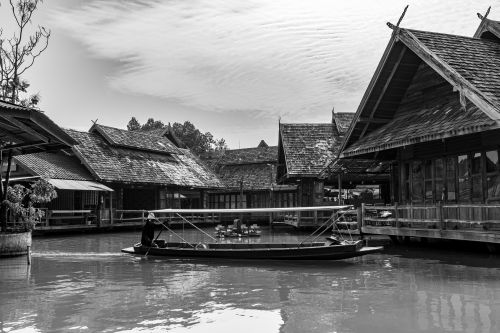 Free A serene black and white capture of a boat along a traditional Thai village by the water. Stock Photo