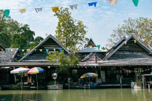 Free Charming floating market with colorful umbrellas and traditional wooden houses reflecting vibrant culture. Stock Photo