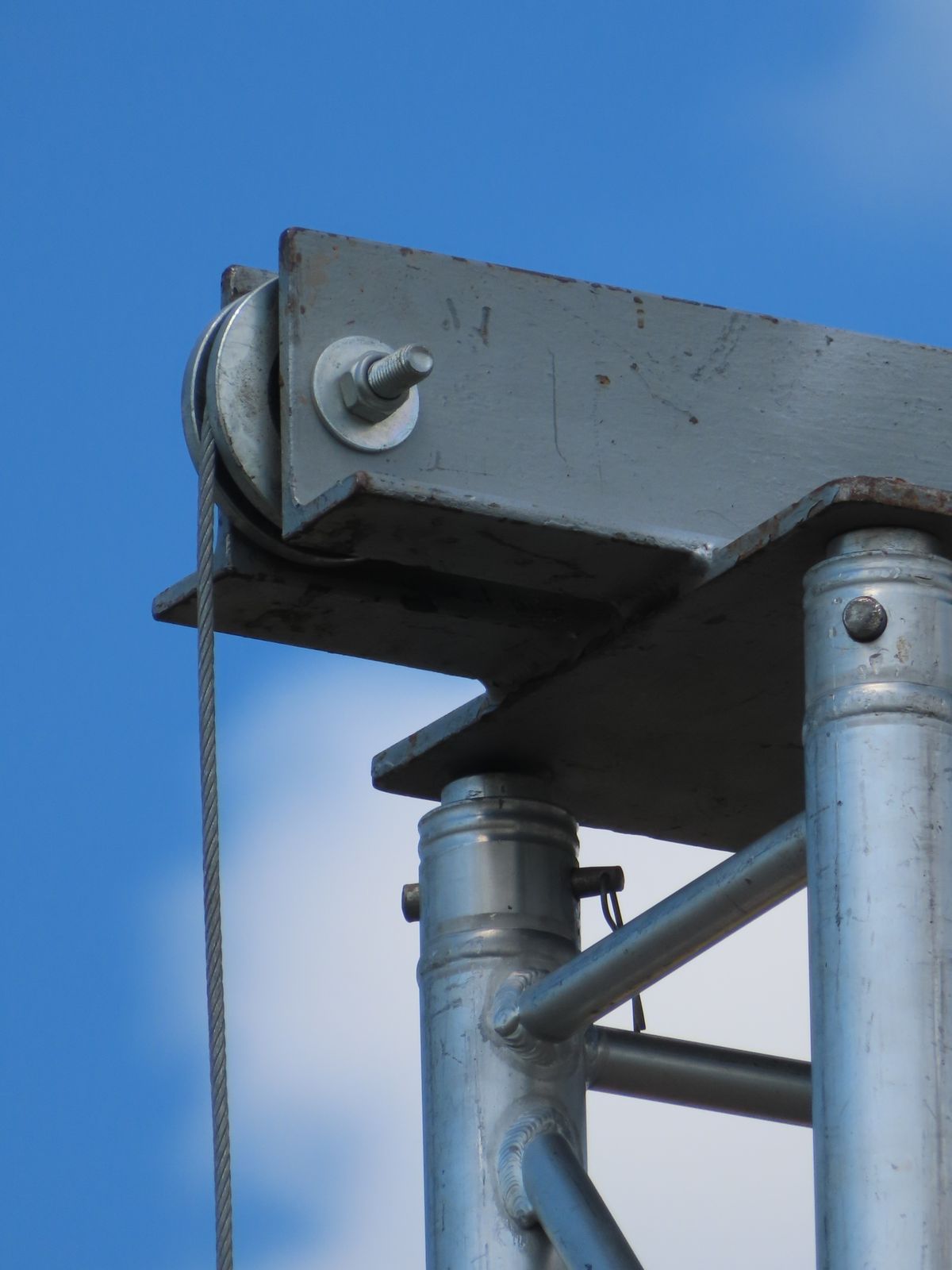 Crane arm with wire rope running over sheave against blue sky