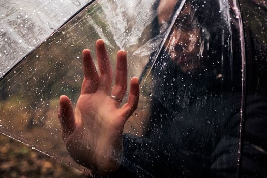 A hand touching a transparent umbrella with raindrops, creating a dramatic outdoor scene.