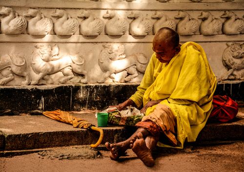 Free A Buddhist monk in yellow robes meditates on a sidewalk, conveying themes of spirituality and simplicity. Stock Photo