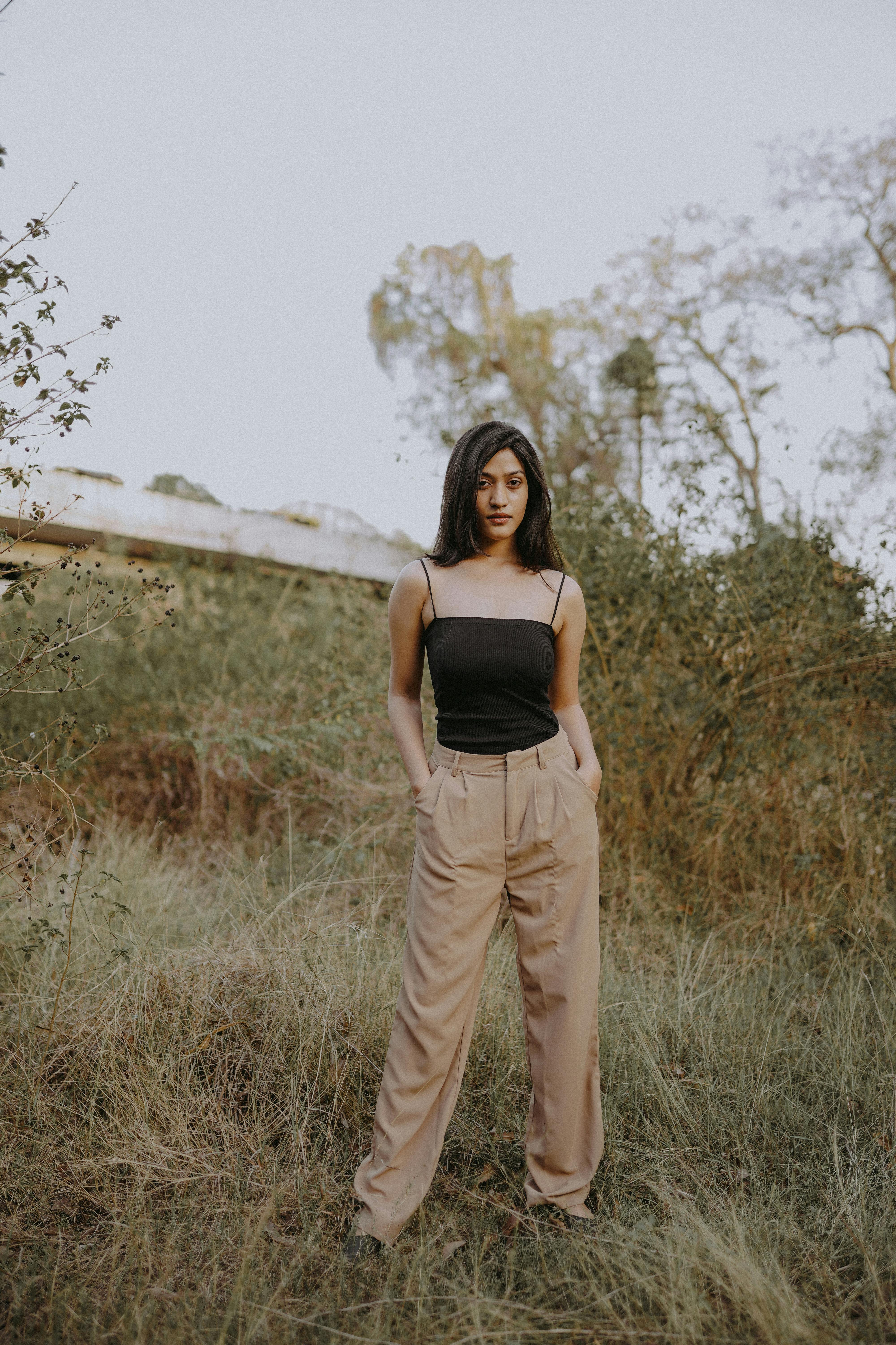 A fashionable woman standing in a natural setting with hands in pockets.