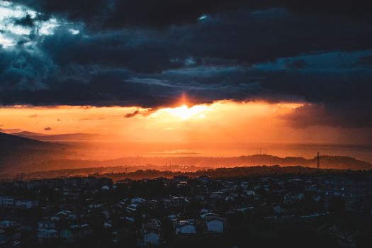 A mesmerizing sunset with dark clouds over a cityscape, capturing a mix of light and shadows.