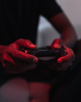 Hands holding a video game controller illuminated by red light in a moody atmosphere.