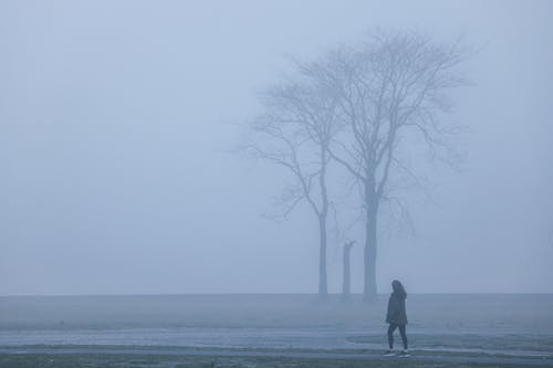 Woman Walking Alone on a Field in Dense Fog