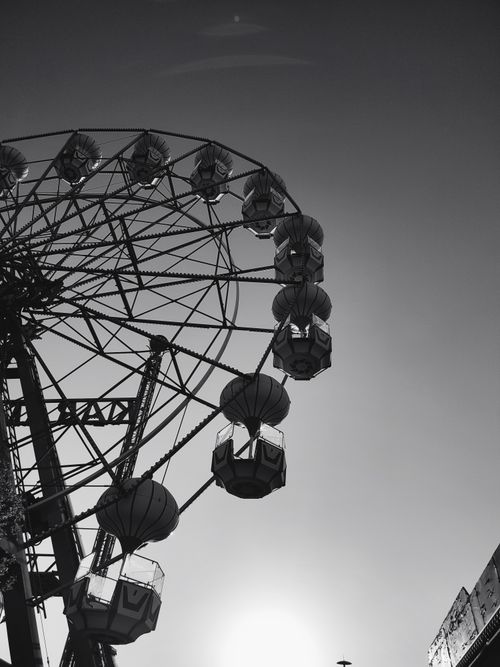 Free Grayscale ferris wheel with a bright sun creating dramatic shadows, captured in low angle. Stock Photo