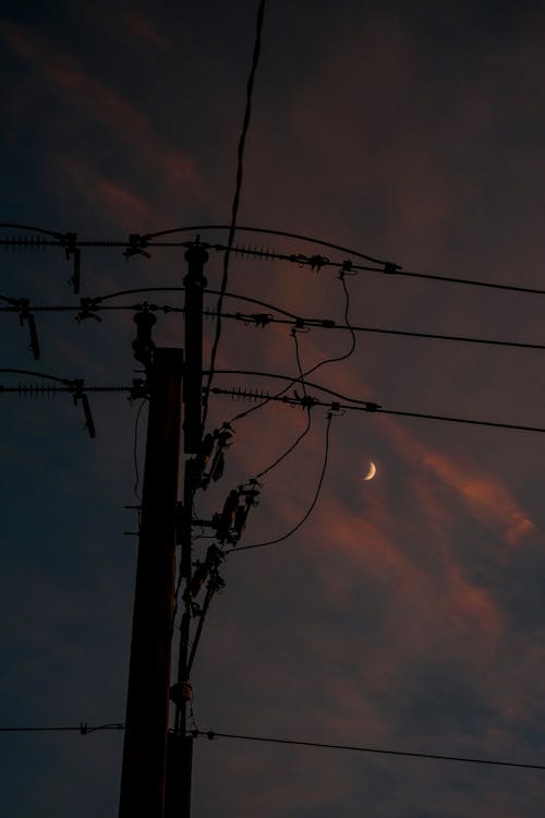 A crescent moon is seen in the sky over power lines