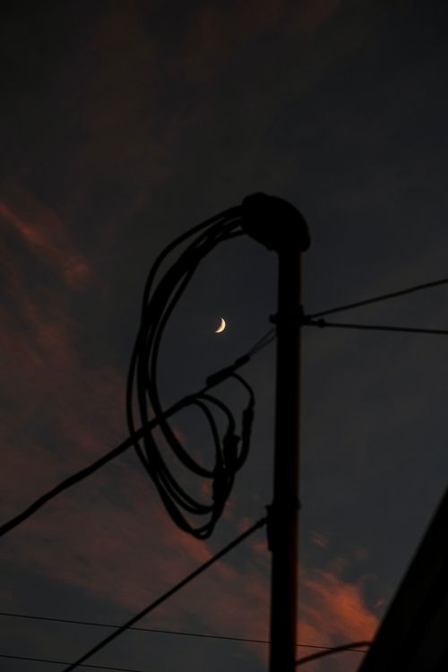 Free Crescent moon framed by silhouetted power lines at dusk, creating a dramatic scene. Stock Photo