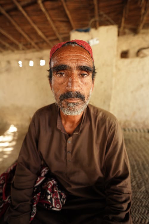 Portrait of an Elderly Man in a Traditional Shirt Sitting Inside 