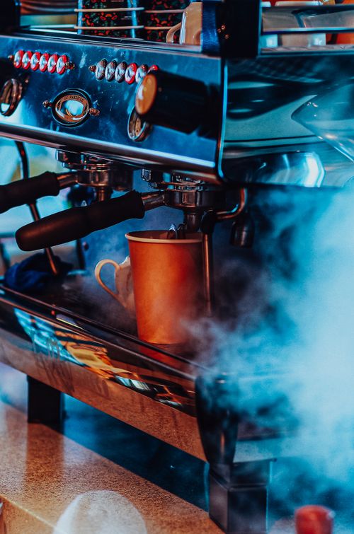 Free Close-up of a steaming mug under an espresso machine in a vibrant café setting. Stock Photo