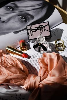Chic arrangement of perfume, lipstick, and jewelry on an open magazine with scarf.
