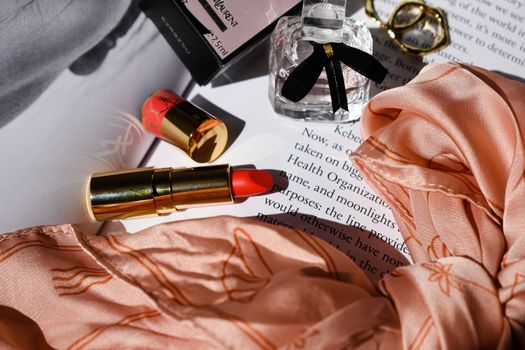Artistic flat lay featuring a vibrant lipstick, elegant perfume, and stylish accessories with a peach scarf.