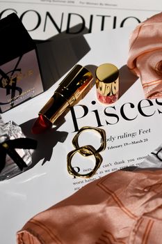 Stylish flat lay featuring gold lipstick and jewelry on a glamorous magazine page.