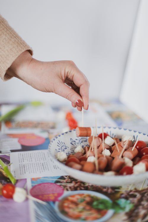 Free A close-up of a hand selecting toothpicked sausage and cheese appetizers from a decorative plate. Stock Photo