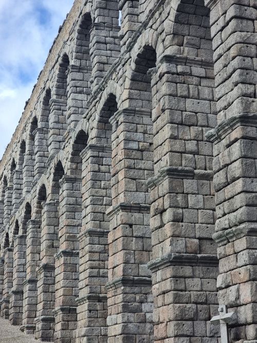 Free Stone arches of the ancient Segovia Aqueduct stretch high under a partly cloudy sky in Spain. Stock Photo