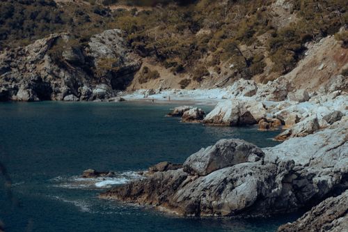Free A tranquil rocky beach with turquoise waters and lush vegetation in the backdrop. Stock Photo