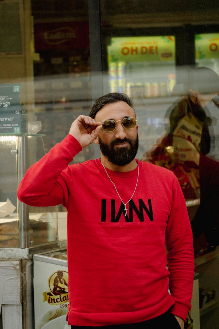 Man In A Red Sweatshirt Fixing His Sunglasses 