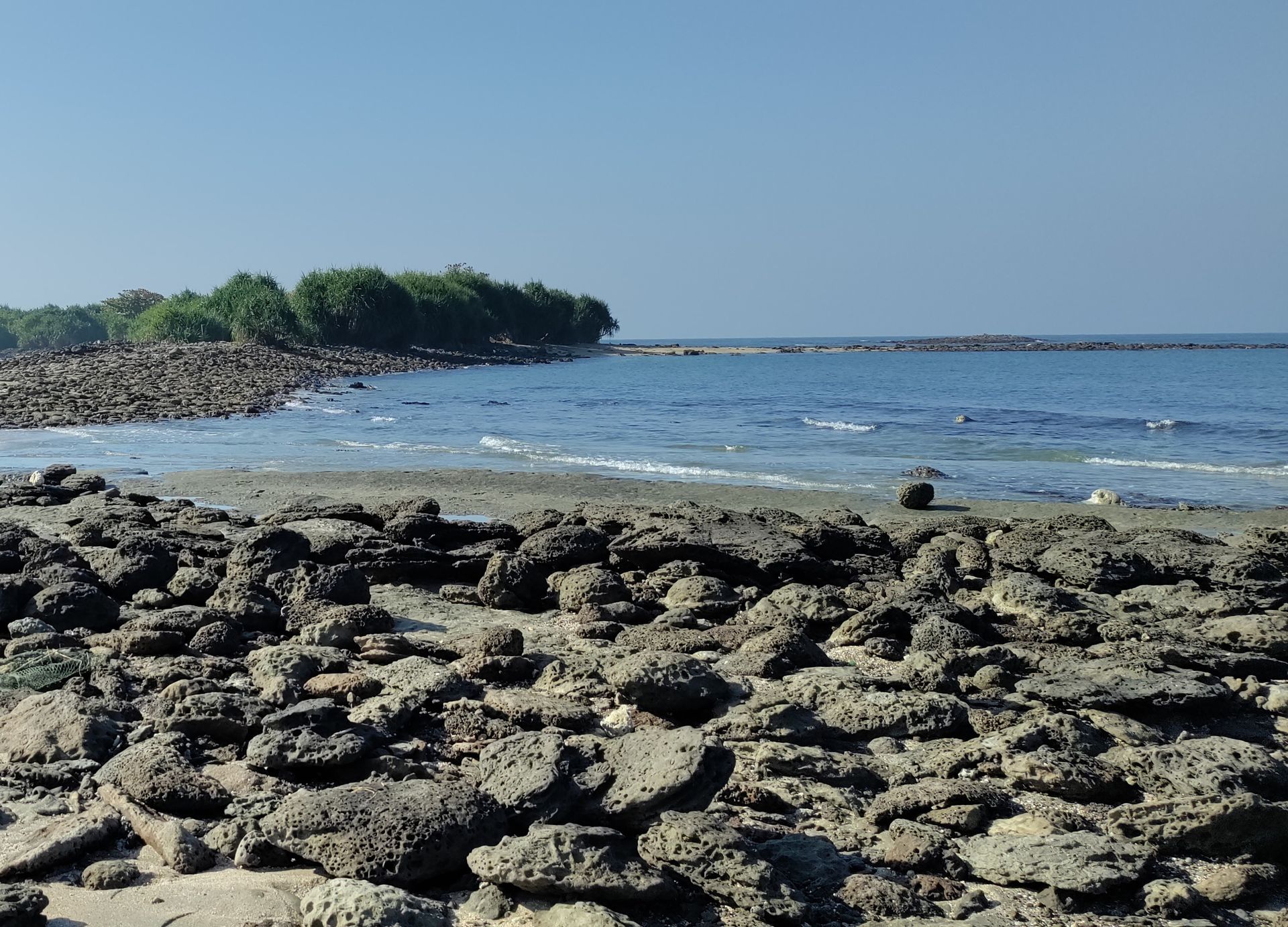 A serene rocky beach in Cox's Bazar, Bangladesh, showcasing lush greenery and clear blue skies.
