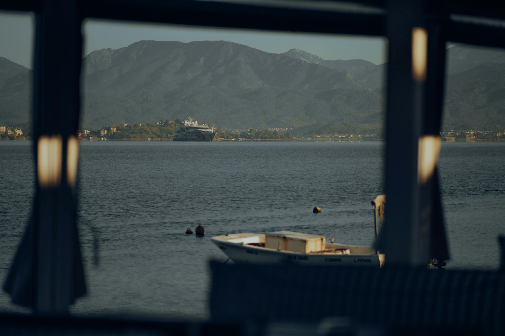 Serene lake scene showcasing a boat, distant ship, and majestic mountains under clear skies.