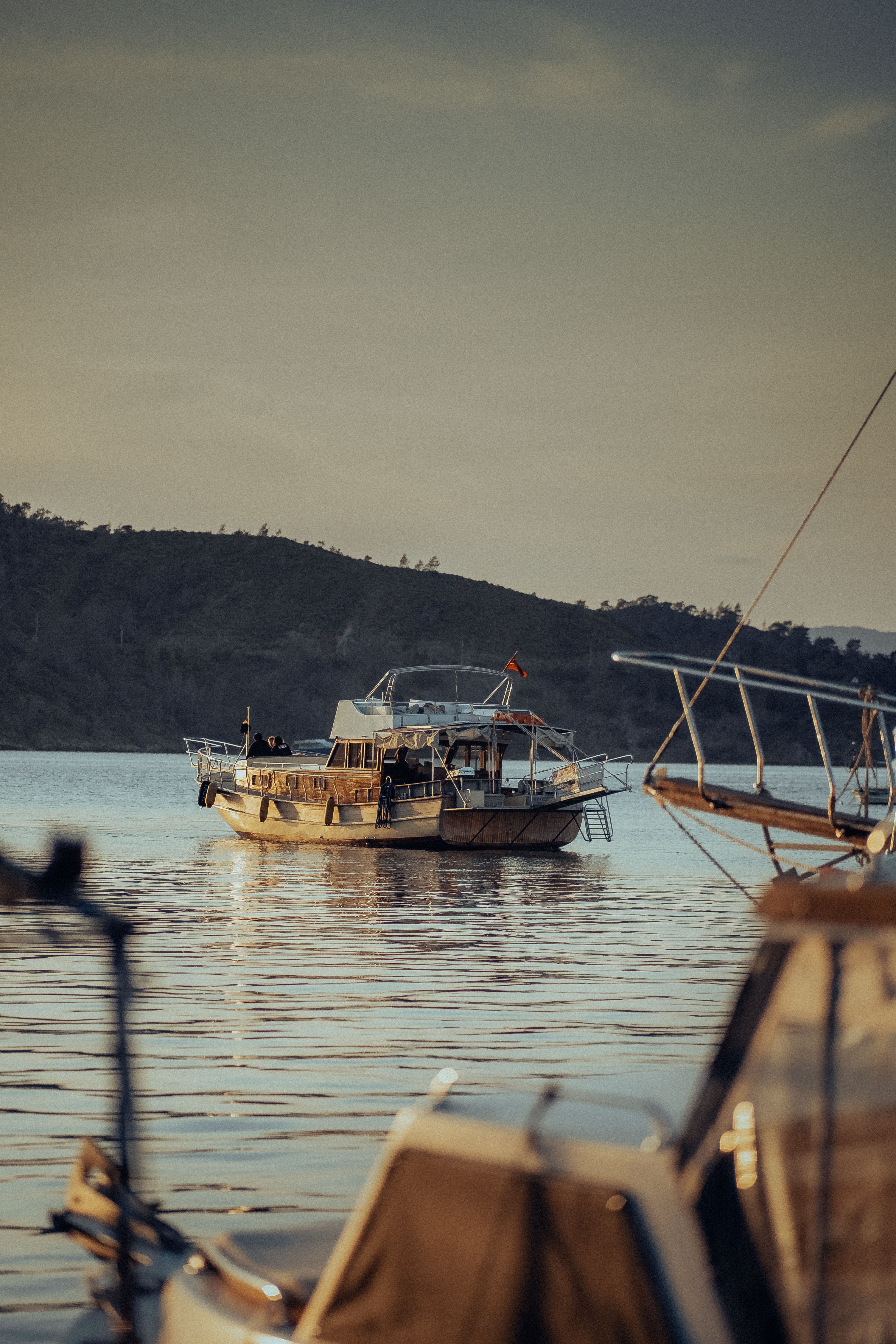 A tranquil scene of a fishing boat on the lake at sunset, framed by nearby boats and hills.