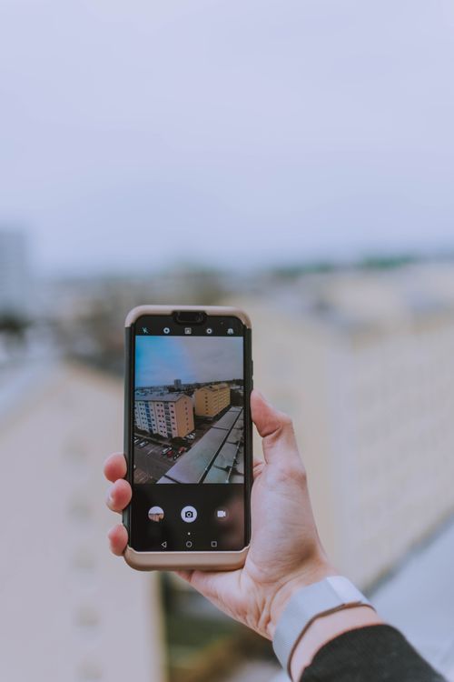 Free Person holding smartphone capturing cityscape view of an urban area. Stock Photo