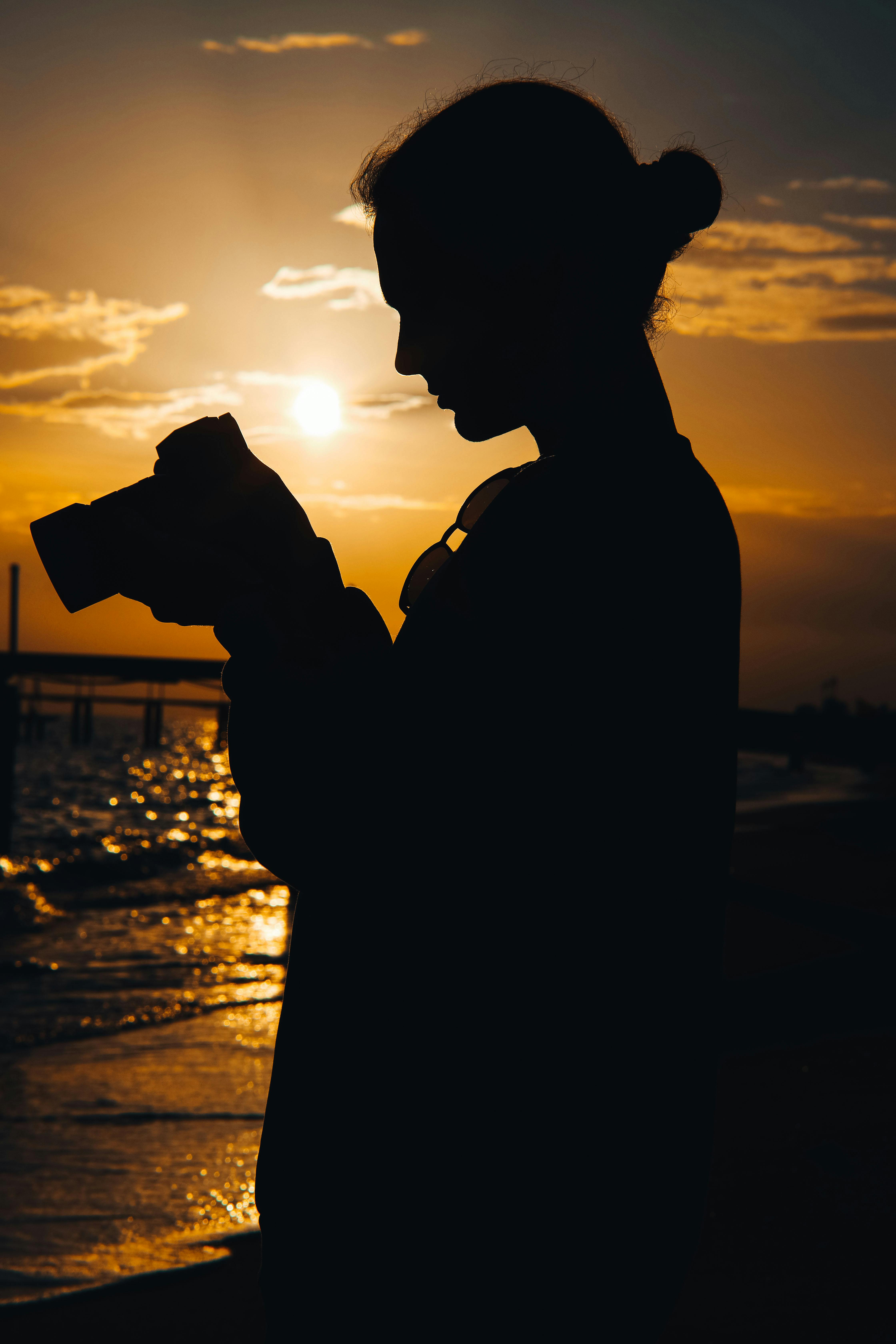 Silhouette of a woman holding a camera on a beach during a stunning sunset by the sea.