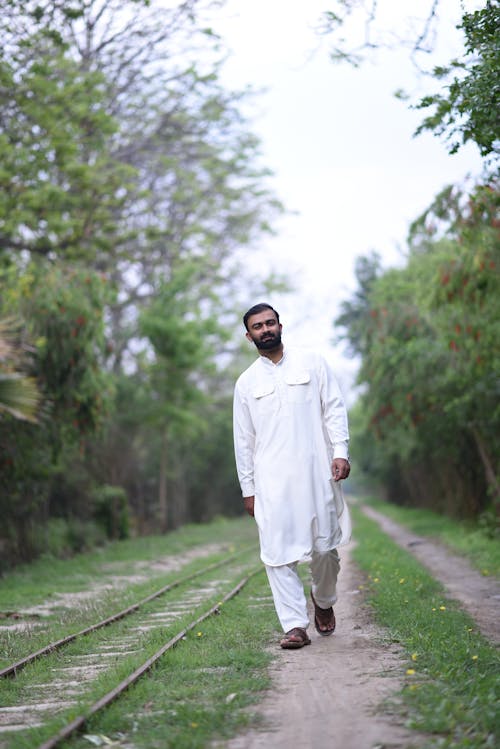 Man in Traditional Clothing Walking on Footpath near Railway